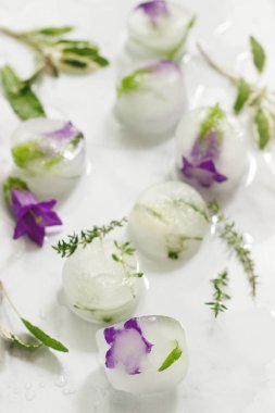 Çiçek ve otlar ışık mermer zemin ile parlak buz küpleri. Seçici odak.