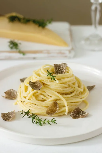 Pasta with creamy cheese sauce and truffle on a light plate, served with cheese and wine. Selective focus.