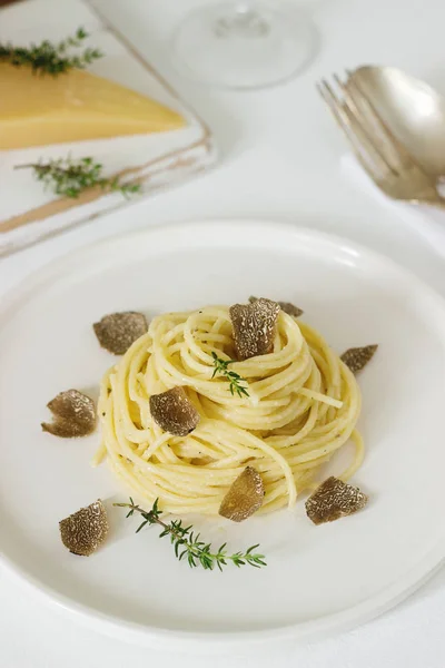 Pasta with creamy cheese sauce and truffle on a light plate, served with cheese and wine. Selective focus.