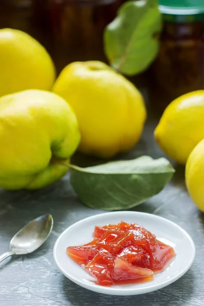 Quittenmarmelade auf einer weißen Untertasse, Quittenfrüchte und Marmeladengläser auf grauem Hintergrund. — Stockfoto