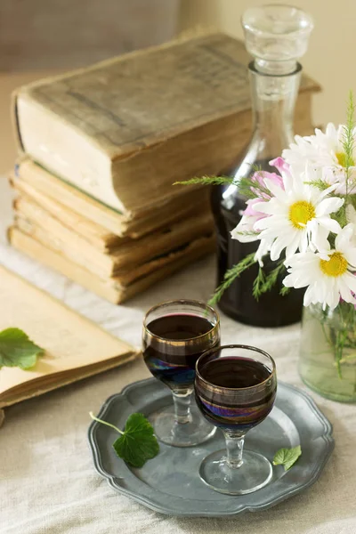 Creme de Cassis hausgemachter Likör aus schwarzen Johannisbeeren in kleinen Gläsern, Büchern und Blumen. rustikaler Stil. — Stockfoto