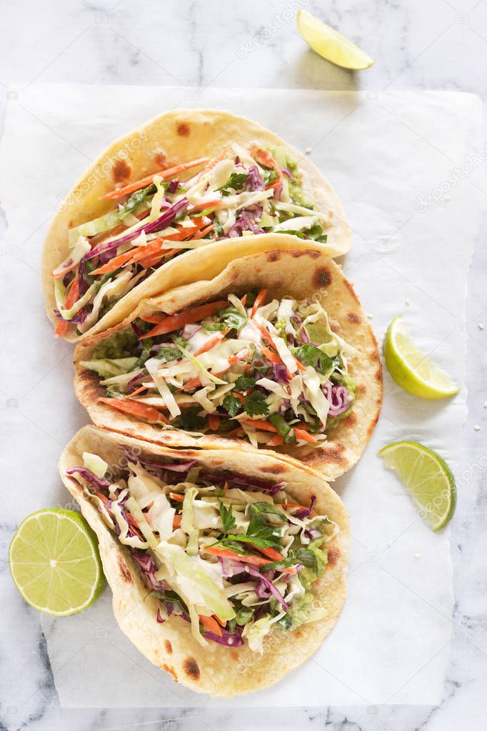 Tacos with guacamole and coleslaw served with lime slices on a light background.