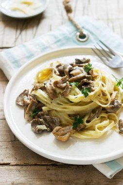 Tagliatelle mantarlı krema ve orman sos ahşap arka plan üzerinde beyaz bir tabak içinde mantar. Rustik tarzı.