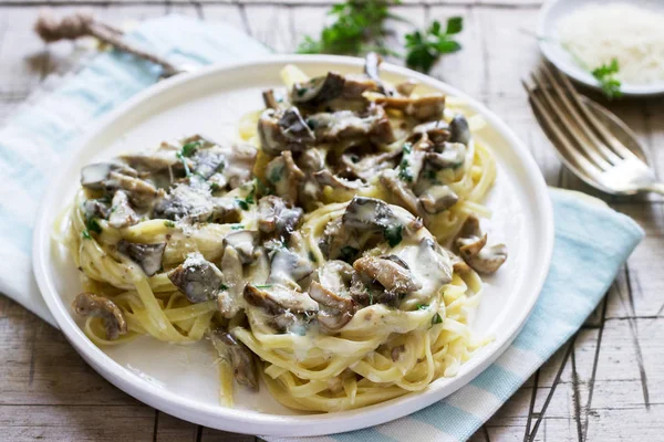 Tagliatelle with cream and forest mushrooms sauce in a white plate on a wooden background. Rustic style, selective focus.