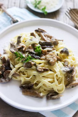 Tagliatelle mantarlı krema ve orman sos ahşap arka plan üzerinde beyaz bir tabak içinde mantar. Rustik tarzı, seçici odak.