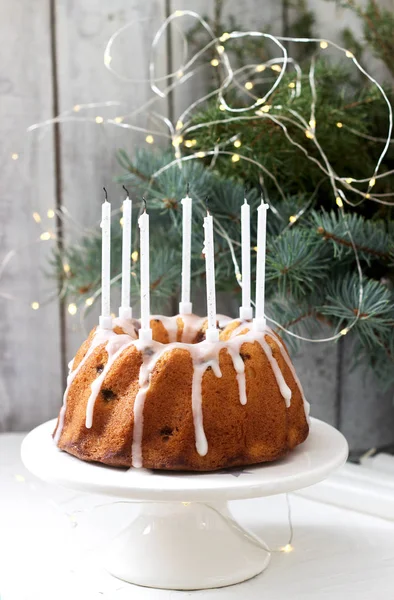 Pie with raisins and icing from powdered sugar on the background of fir branches and garlands. Rustic style. — Stock Photo, Image