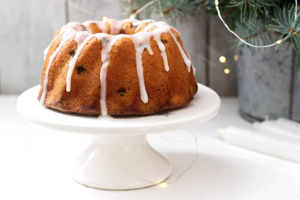 Pie with raisins and icing from powdered sugar on the background of fir branches and garlands. Rustic style, selective focus.