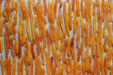 Candied orange peel, cooked in sugar syrup with vanilla and ginger, drying on parchment. Selective focus. clipart