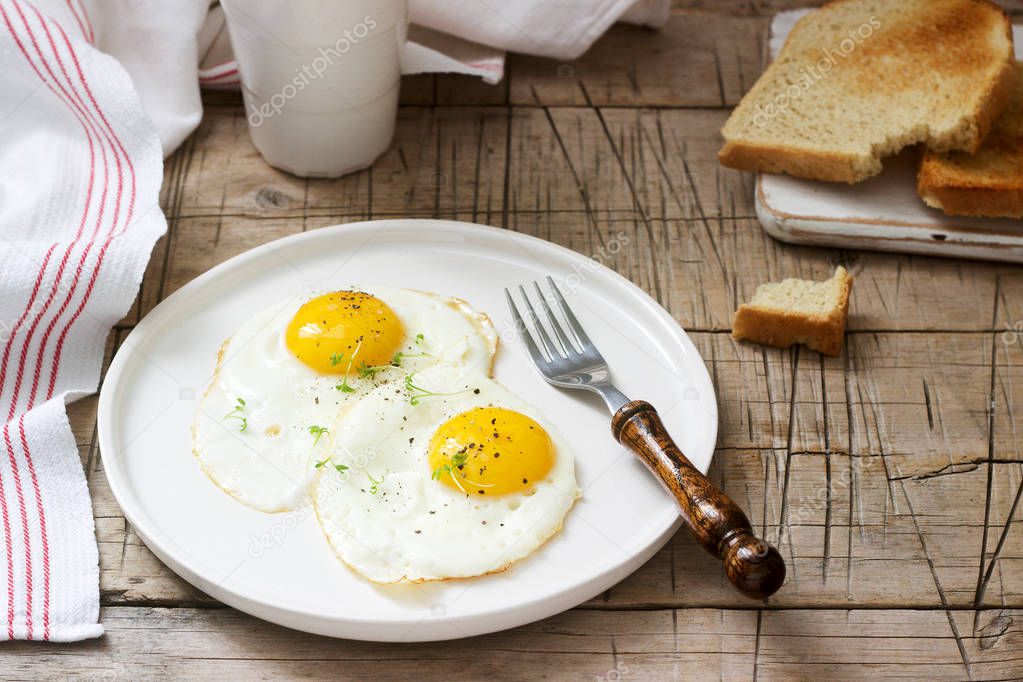 Breakfast of fried eggs, bread toasts and coffee on a wooden table. Rustic style, selective focus.
