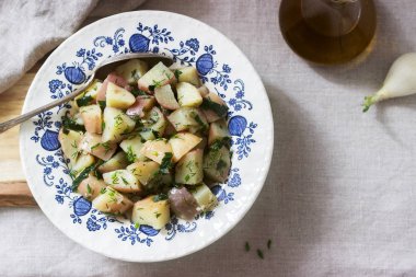Geleneksel soğuk patates salatası soğan ve keten masa örtüsü arka plan üzerinde otlar. Rustik tarzı.