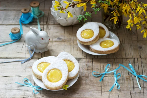 Пасхальная композиция с яйцеобразным печеньем, наполненным лимонным творогом, кроликом, букетом форсайта и луками . — стоковое фото