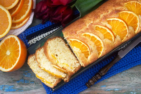 Orange cake, decorated with slices of orange on a background of juicy oranges and a bouquet of tulips. Rustic style.