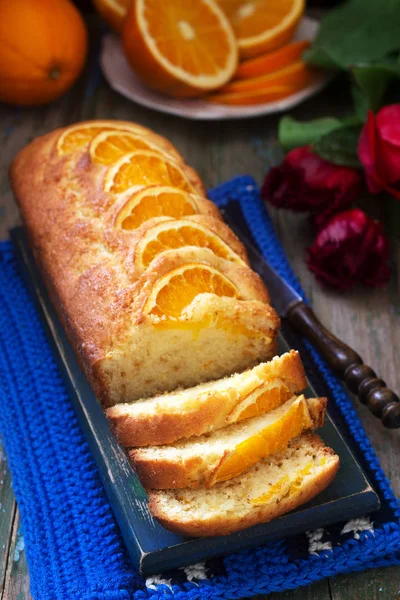 Orange cake, decorated with slices of orange on a background of juicy oranges and a bouquet of tulips. Rustic style.