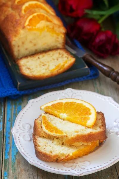 Помаранчевий торт, прикрашений скибочками апельсина на тлі соковитих апельсинів і букетом тюльпанів. русичний стиль . — стокове фото