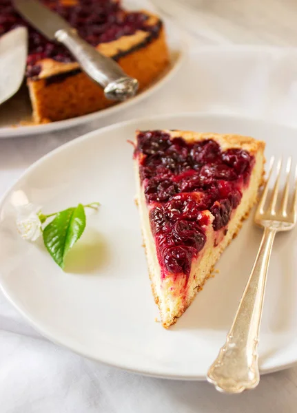 Homemade cherry pie served with cream on a light background with cherry leaves and flowers.