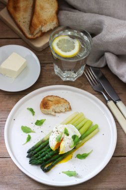 Ahşap bir yüzeyde tereyağı ve marul ile haşlanmış yumurtalı ve pişmiş kuşkonmamış kahvaltı. Rustik tarzı.