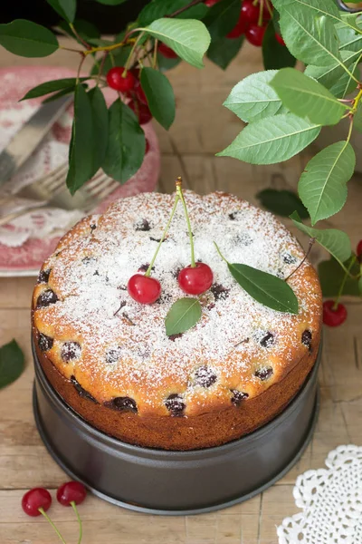 Вишневый пирог, посыпанный сахарной пудрой на деревянный стол на фоне вишневых ветвей. Сельский стиль . — стоковое фото