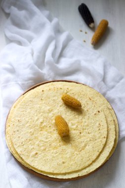 Tahta bir tahta ve mısır koçanları üzerinde yuvarlak mısır tortilla yığını.