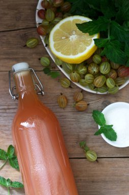 Bir cam şişe ve ahşap bir masada şurup için malzemeler bektaşi üzümü, limon ve nane şurubu.