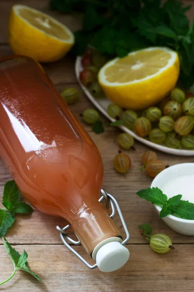 Stachelbeer-, Zitronen- und Minzsirup in einer Glasflasche und Zutaten für Sirup auf einem Holztisch. — Stockfoto