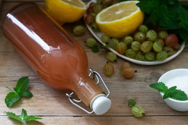 Stachelbeer-, Zitronen- und Minzsirup in einer Glasflasche und Zutaten für Sirup auf einem Holztisch. — Stockfoto