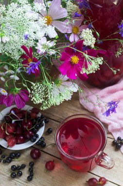 Bir cam fincan, çilek ve bir deoanean arka planda vahşi çiçekler bir buket Berry kompostosu. Rustik tarzı.