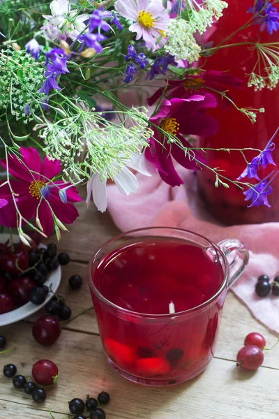 Compote de baies dans une tasse en verre, baies et un bouquet de fleurs sauvages sur un fond de décanéen. Style rustique . — Photo