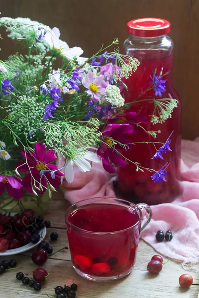 Compote de baies dans une tasse en verre, baies et un bouquet de fleurs sauvages sur un fond de décanéen. Style rustique . — Photo