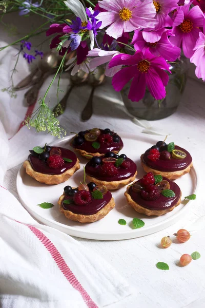 Shortbread tartlets with berry custard and flowers on a light background. — Stock Photo, Image