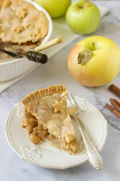 A traditional American apple pie decorated with stars and sugar, apples and cinnamon on a light background.