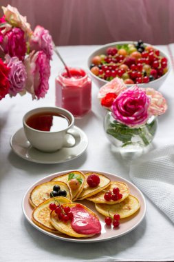 Çayla servis edilen çilekli krep ve gül buketleriyle süslenmiş bir masa. Seçici odak.