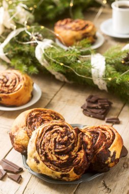 Salyangoz çikolatalı kekler köknar dalları ve koni çelenklerinin arka planında kahveyle servis ediliyor. Kırsal biçim, seçici odak.