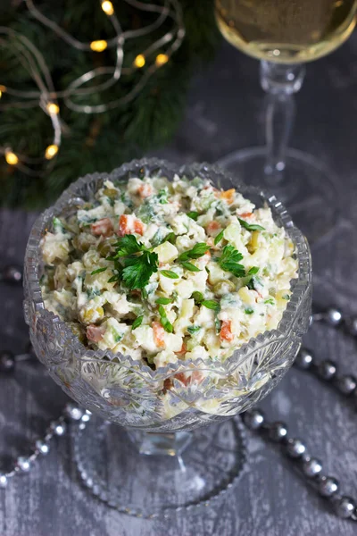 Salată tradițională festivă Olivier într-o vază de cristal, servită cu vin alb pe fundalul decorațiunilor de Crăciun . — Fotografie, imagine de stoc