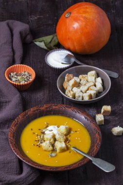 Kabak kremalı çorba, kızarmış ekmek, krema ve tohumla servis edilir. Koyu bir ahşap masada sonbahar sebze çorbası. Kırsal biçim, seçici odak.