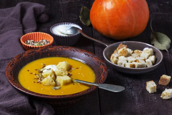 Kabak kremalı çorba, kızarmış ekmek, krema ve tohumla servis edilir. Koyu bir ahşap masada sonbahar sebze çorbası. Kırsal biçim, seçici odak.