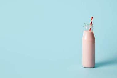 Çilekli milkshake içme saman üzerinde mavi arka plan ile şişe 