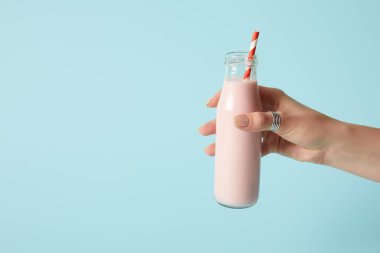 Çilekli milkshake içme saman üzerinde mavi arka plan ile şişe tutan kadın görüntüsünü kırpılmış 