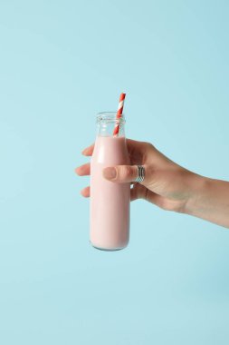 Çilekli milkshake içme saman üzerinde mavi arka plan ile şişe tutan kadın kırpılmış görüntü 