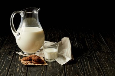 closeup view of fresh milk in jug and glass, chocolate cookies and sackcloth on black background  clipart