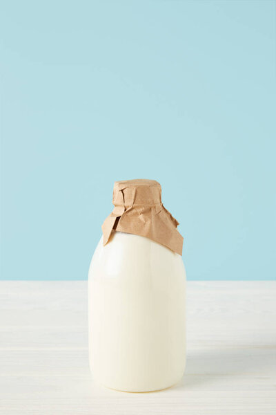 closeup view of fresh milk in bottle wrapped by paper on blue background 