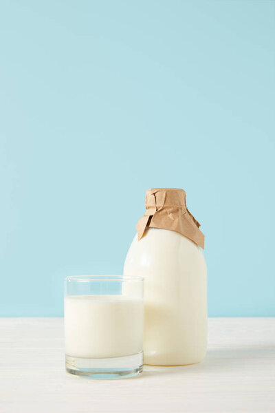 closeup shot of milk glass and milk in bottle wrapped by paper on blue background 