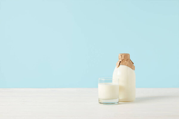 milk glass and milk in bottle wrapped by paper on blue background 
