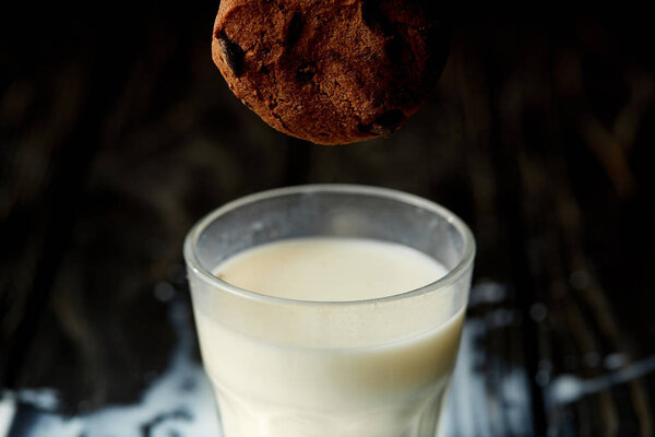 closeup view of chocolate cookie falling into glass with milk 