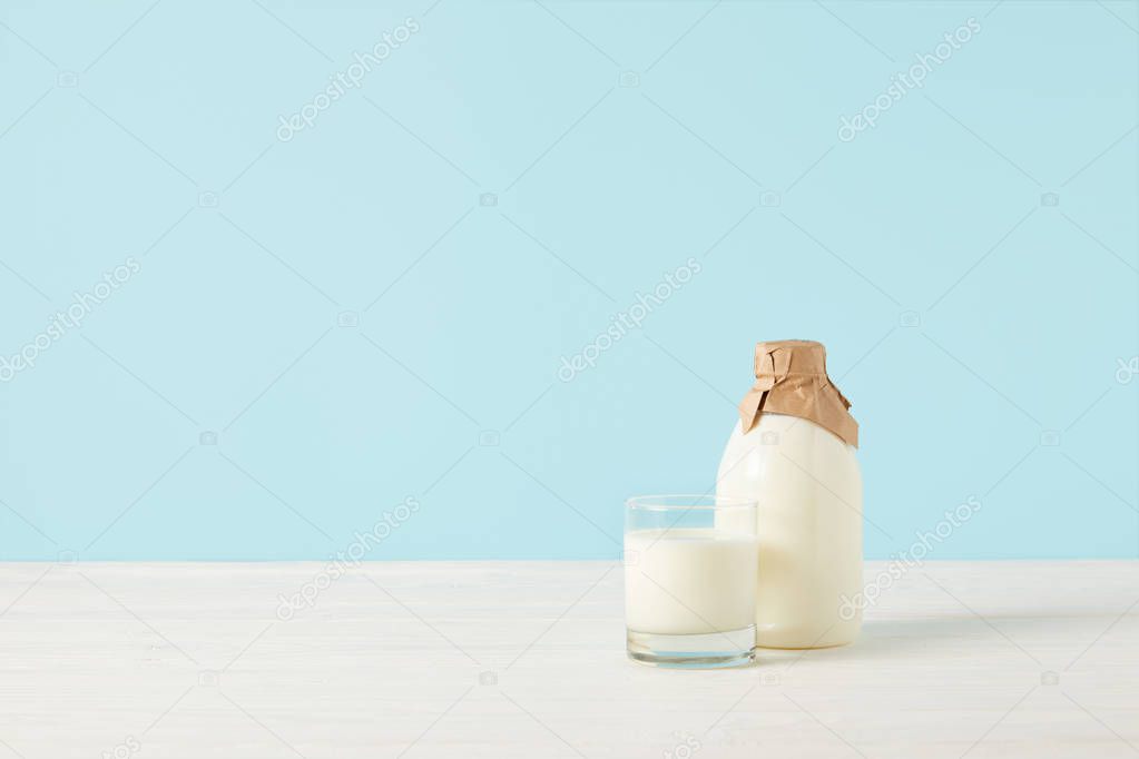 milk glass and milk in bottle wrapped by paper on blue background 