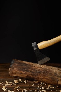 close up view of sticking axe in log and wooden chips on black background  clipart