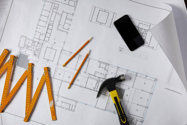 top view of hammer, collapsible meter, pencils and smartphone with blank screen on blueprint