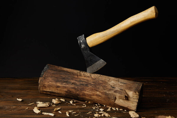 log with sticking axe and wooden pieces at table on black background