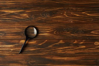 top view of single black magnifying glass with handle on wooden table clipart