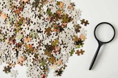 top view of magnifying glass and jigsaw puzzle pieces on grey 