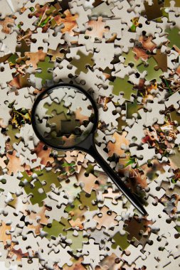 top view of magnifying glass and jigsaw puzzle pieces on grey  clipart